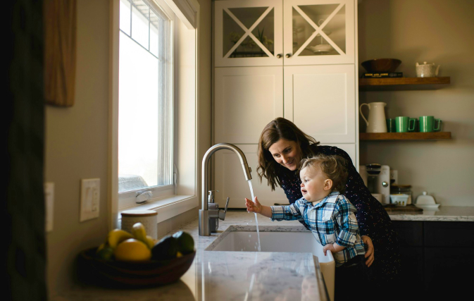 woman and child playing with water from a tap